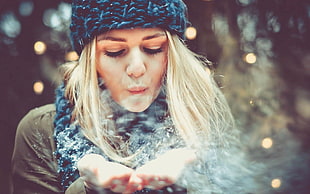 woman wearing winter clothing while blowing snow off her hands