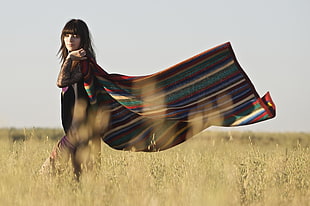 woman in red and green stripe poncho standing on green grass field, mallorca
