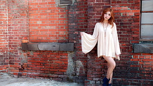 woman wearing white trumpet-sleeved dress standing against red brick wall