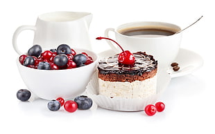 cupcake with cherry topping near filled white cup on saucer, white pitcher, and bowl of cherries