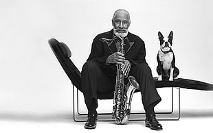 grayscale photo of man holding trombone near dog