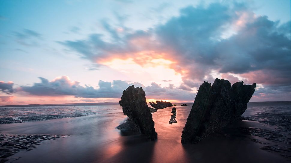 silhouette of two formation of rocks on seashore HD wallpaper