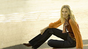 woman with black flare jeans, brown blouse with brown cardigan and black leather chunky-heeled boots outfit sitting on brown concrete pavement