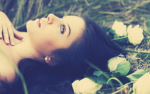 shallow focus on black haired woman laying on grass surrounded by flowers