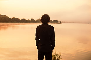 silhouette photo of man beside calm body of water