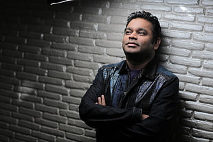 man wearing black dress shirt leaning on wall
