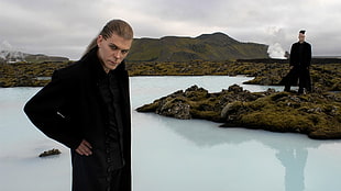 man in black coat standing near body of water