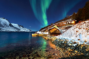 aurora borealis photo of house near of bodies of water near of mountain