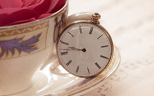 gold-colored pocket watch on top of white saucer near cup