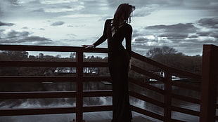 woman wearing long sleeve long dress facing side beside fence under white and grey clouds