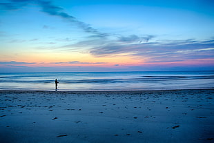 photo of person standing near ocean during golden hour