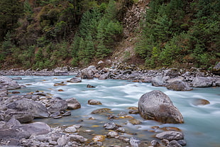 photography of rocks on river beside mountain slope