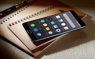 black smartphone on two beige spiral notebooks