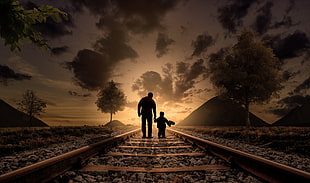 Silhouette of man and boy walking on the railway