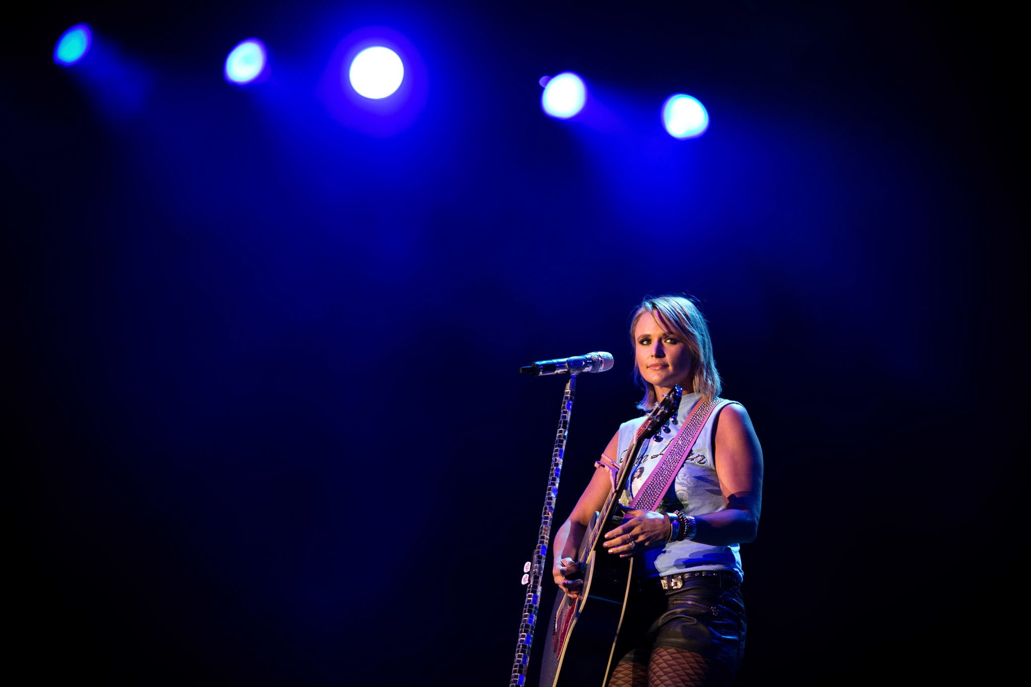 woman stands on stage playing guitar and using microphone with blue lights