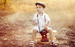 boy in white button-up shirt sitting on chair while holding camera during daytime
