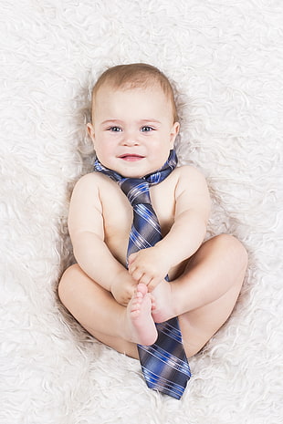 baby wearing necktie laying on The bed