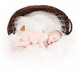 baby sleeping on white textile near basket