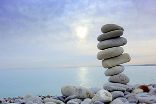 person taking photo of stacked stones with body of water during daytime HD wallpaper