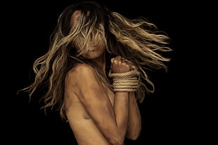 photo of woman with both of her hands tied in brown rope with dark background