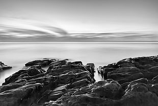 gray scale photography of body of water beside rocks