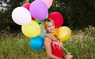 woman holding assorted colors of balloons and wearing red spaghetti strap