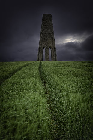 tower on grass field under the stormy clouds