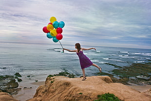 woman standing on the rock cliff holding balloons