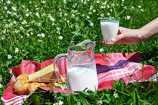photography clear glass pitcher with milk with person's hand holding glass with milk