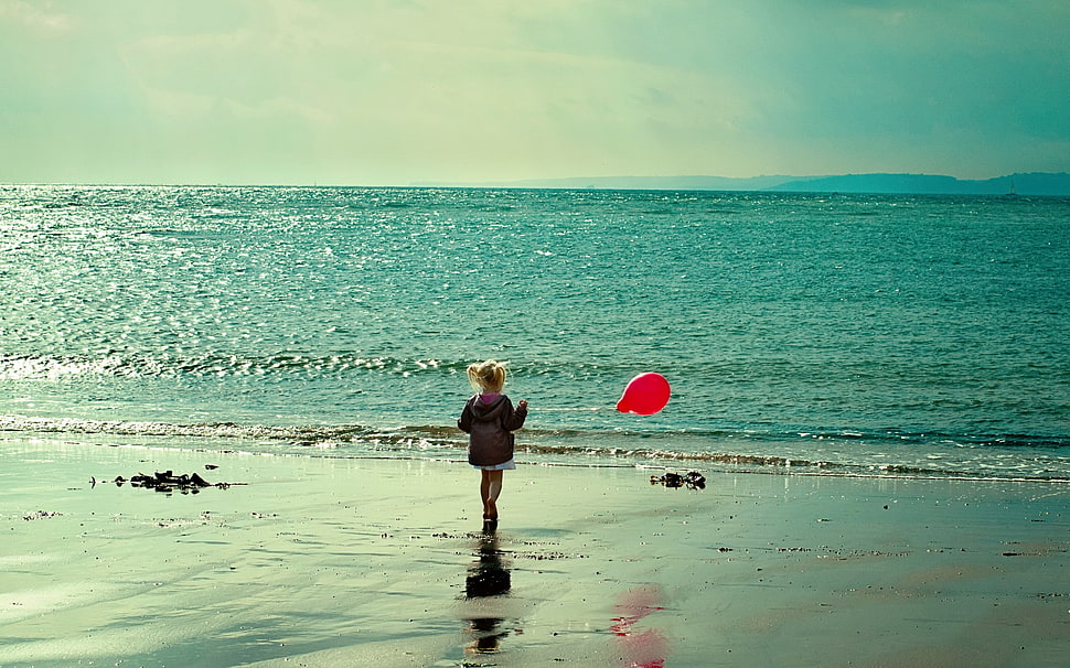 girl holding red balloon standing in sea shore during day time HD wallpaper