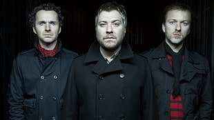 three men in black double-breasted coats posing for a photo