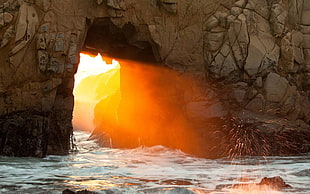 photo of body of water between tunnel, sunlight, rock, arch, sea