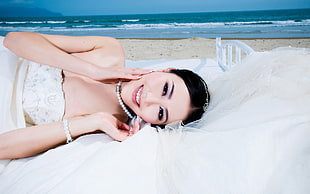 woman in white wedding dress with necklace lying on white textile