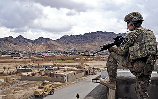 soldier in camouflage uniform standing on the top of the building holding rifle