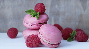 three pink French macaroons surrounded by raspberries
