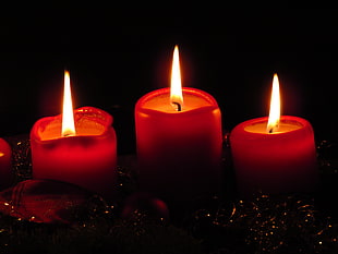 three lighted red pillar candles in black room