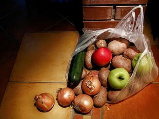 brown potato, green apple, brown onion, red tomato and green cucumber in plastic bag on brown wooden table