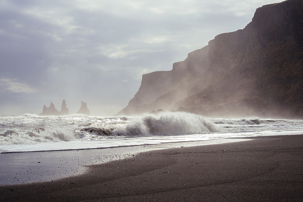 sea near mountain at daytime HD wallpaper