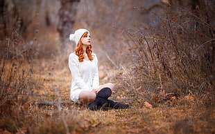 woman in white long-sleeved shirt and black knee-high boots sits on wood ruding daytime