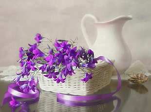white wicker basket of purple Petunia flowers beside white ceramic pitcher on table