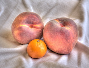 peach fruit and orange fruit on white textile