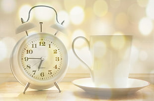 white alarm clock beside a white coffee mug