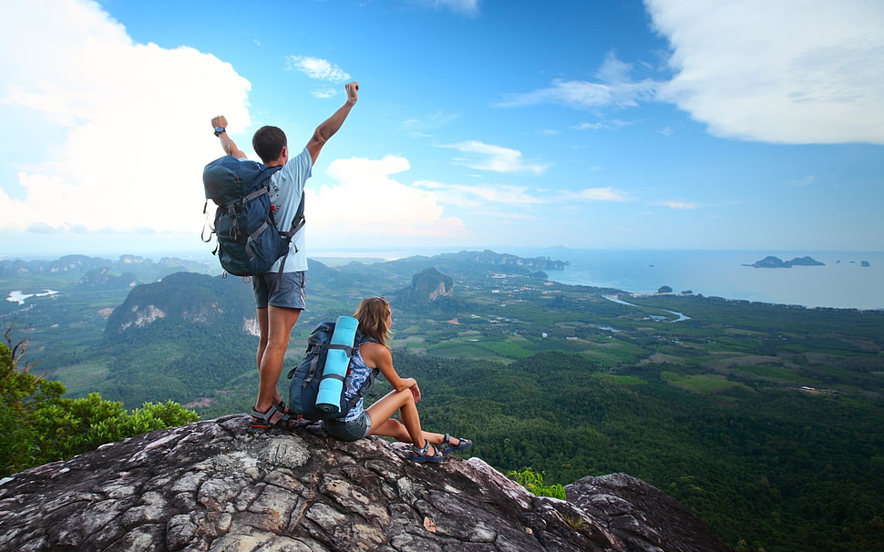 man and woman sitting and standing on mountain  during white cloudy sky HD wallpaper