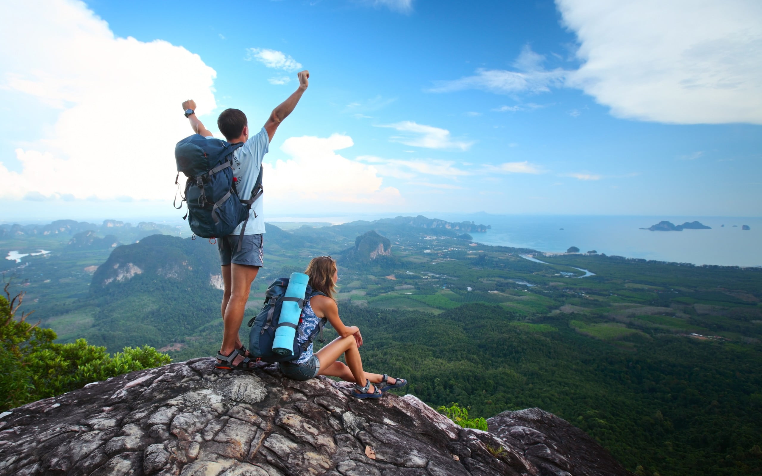 man and woman sitting and standing on mountain  during white cloudy sky