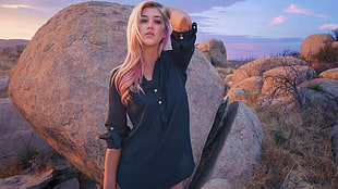 woman wearing black mid-button long-sleeved blouse standing beside gray rock under blue and orange sky