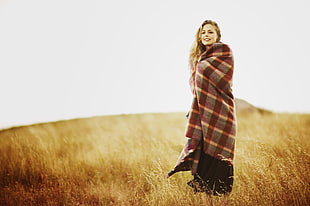 woman in a grassfield covering herself with a plaid print sheet
