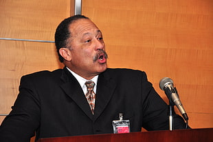 man wearing formal suit speaking in front of microphone