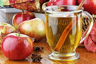 red apples near clear glass mug with brown beverage