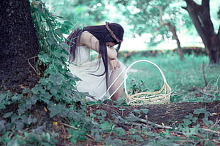 woman wearing white dress sitting near a brown wicker basket