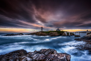 lighthouse on island connected with white bridge on sea under dramatic clouds HD wallpaper